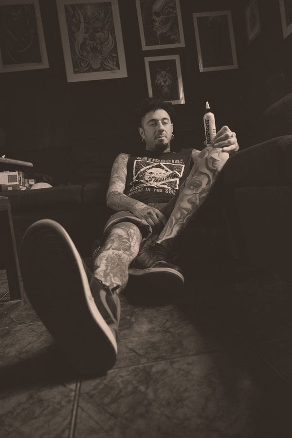 Bruno Moretti seated among his framed dark-art prints, holding a bottle of Radiant tattoo ink